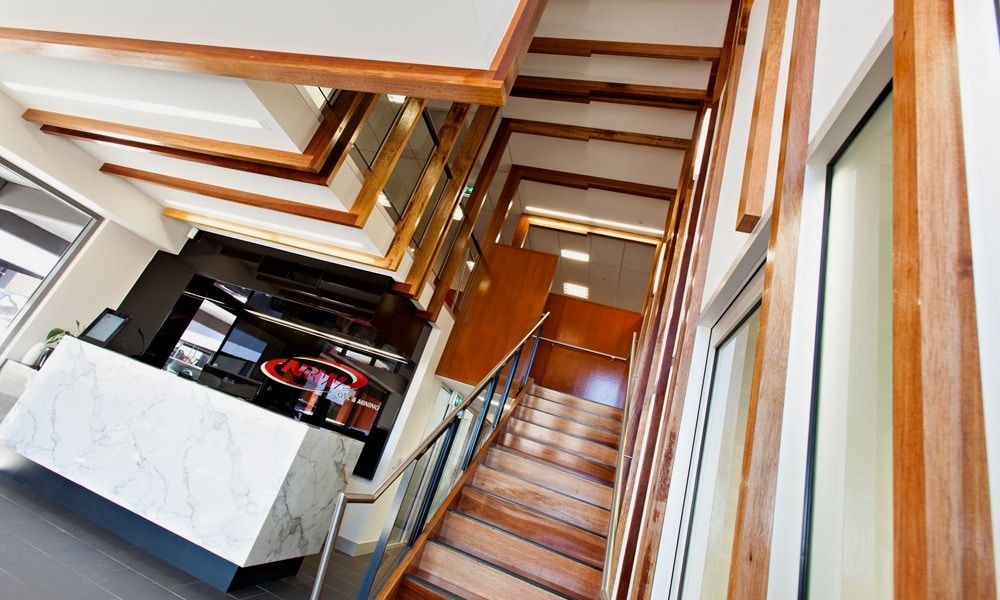 Wooden Staircase With Surrounding Beams, Leading Up to an Office Reception Area With a Marble Counter — BOLD Architecture + Interior Design In Mackay, QLD