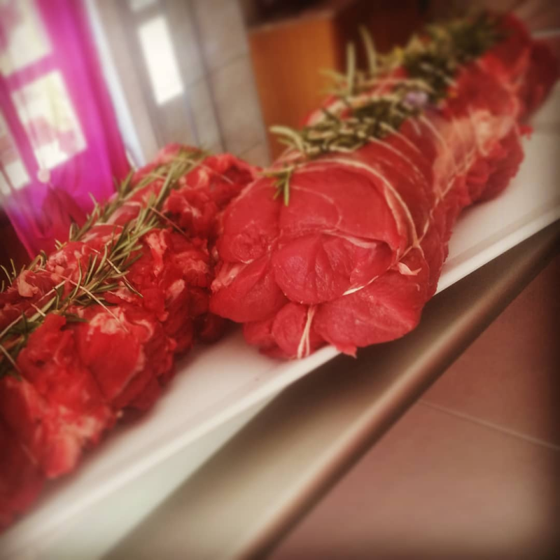 Filetto di manzo crudo legato con spago, guarnito con rametti di rosmarino, su un piatto rettangolare bianco.