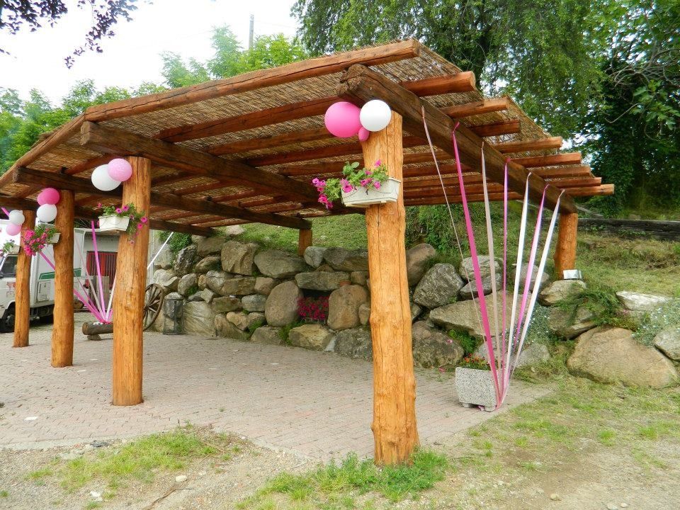 Pergolato in legno decorato con palloncini e nastri rosa e bianchi, fiori e uno sfondo in pietra.