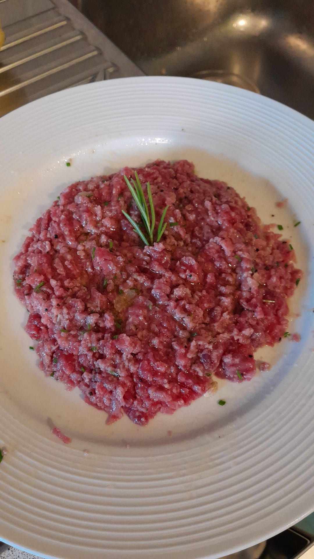 Tartare di manzo su un piatto bianco, guarnita con rosmarino.