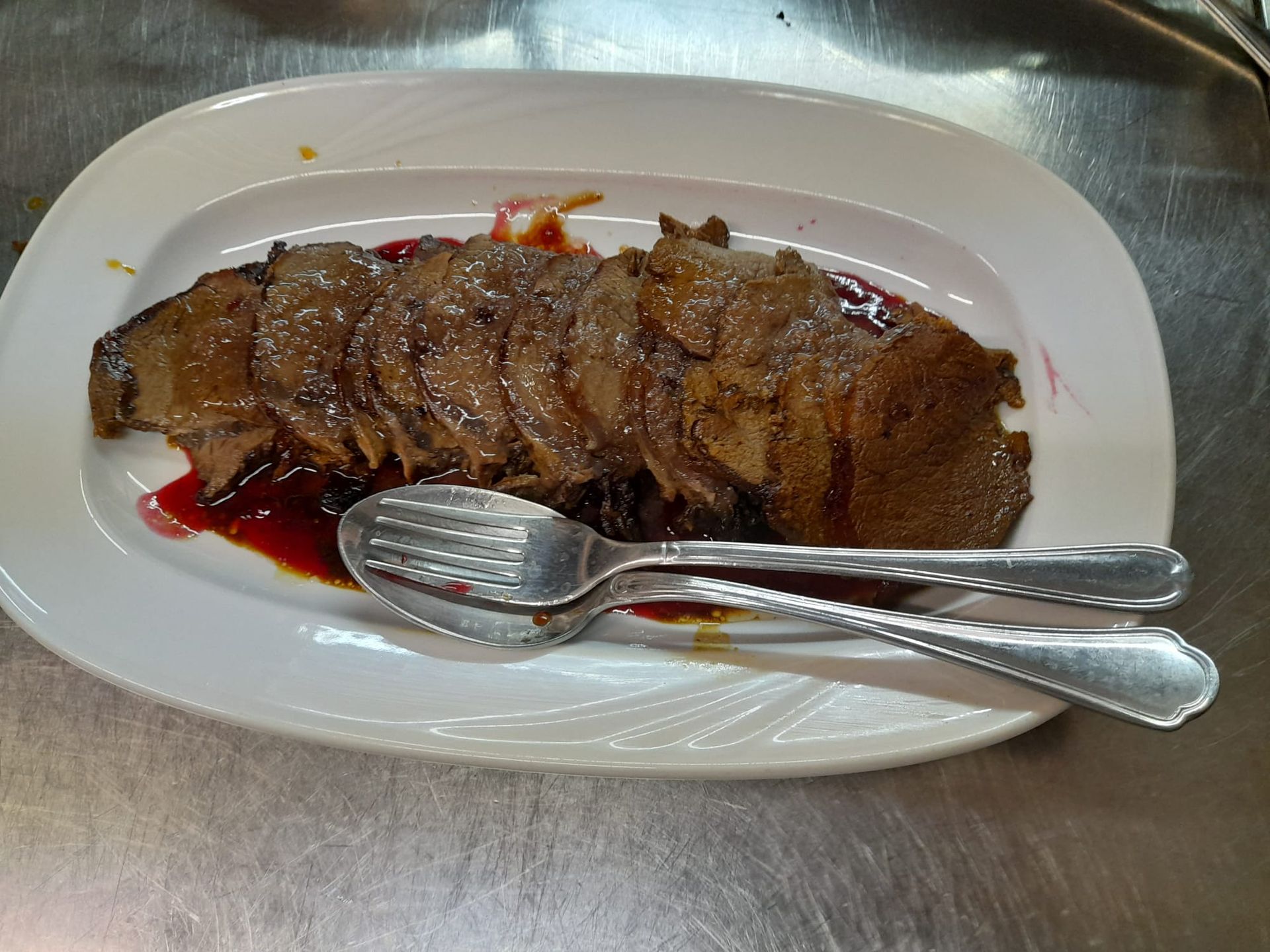 Roast beef affettato con salsa su un piatto bianco con posate.