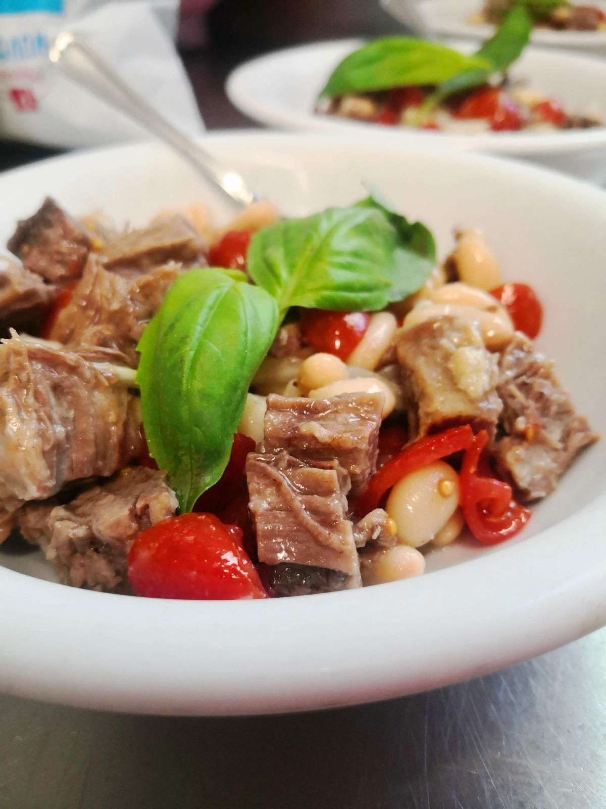 Ciotola di carne cotta con fagioli e pomodori, guarnita con basilico.