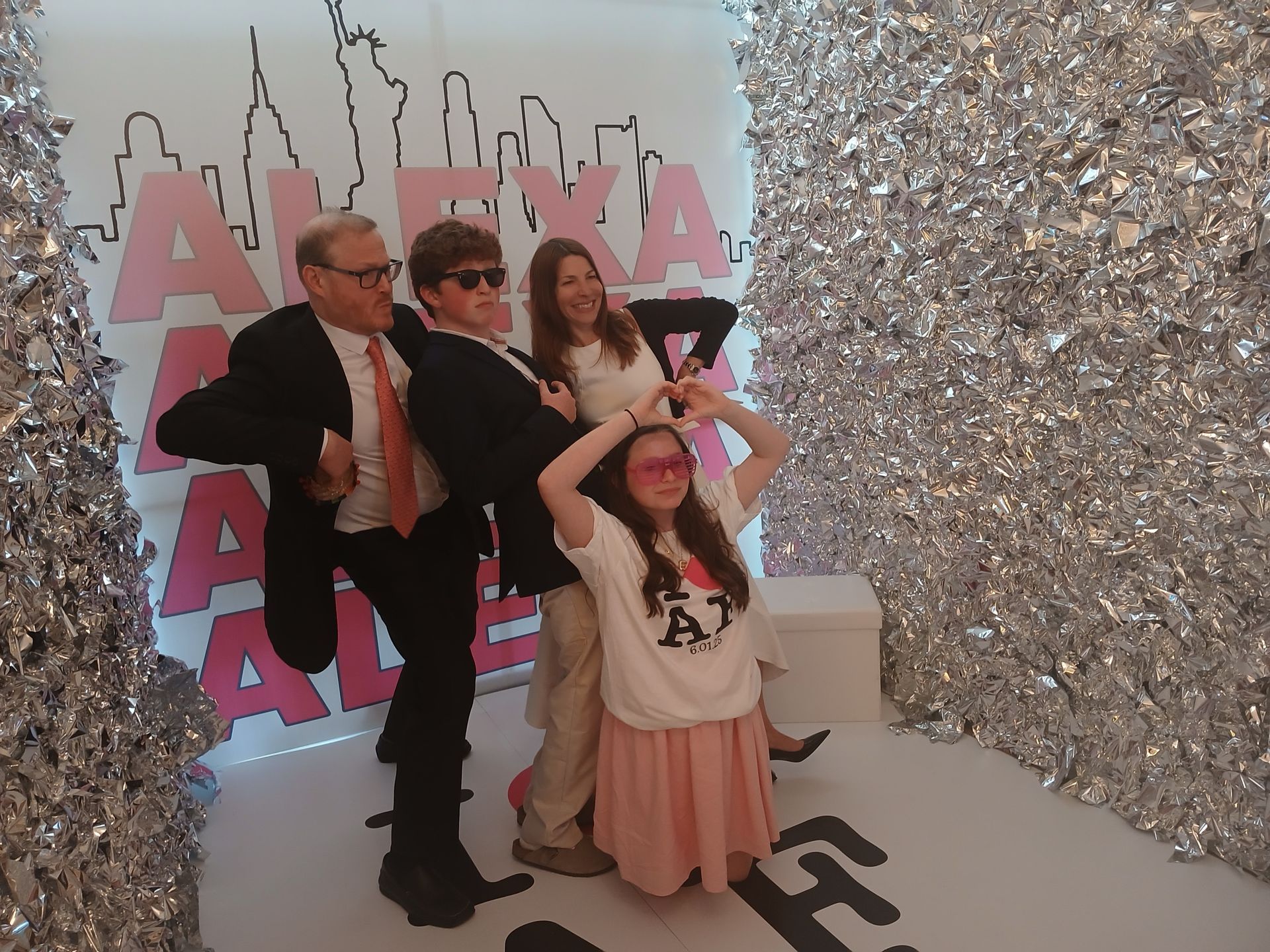 Group poses in a photo booth with silver streamers, pink accents, and New York City outline.