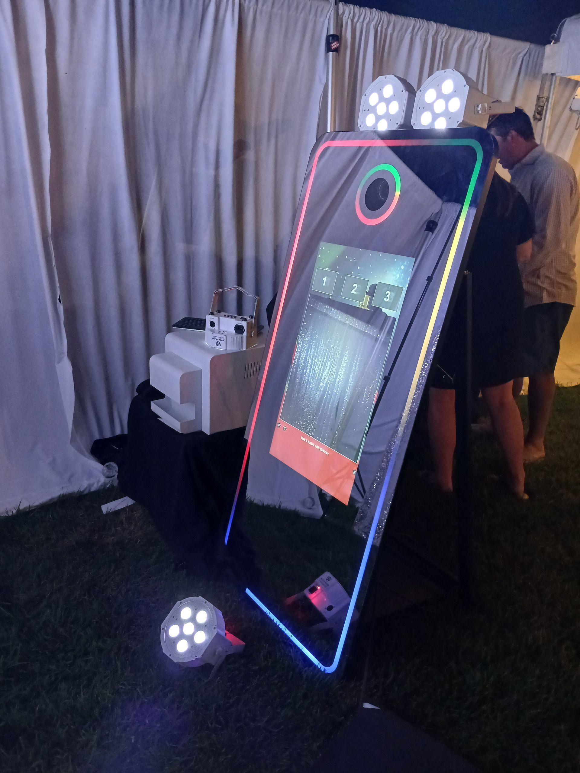 Photo booth with LED lights at an event. A person stands nearby.