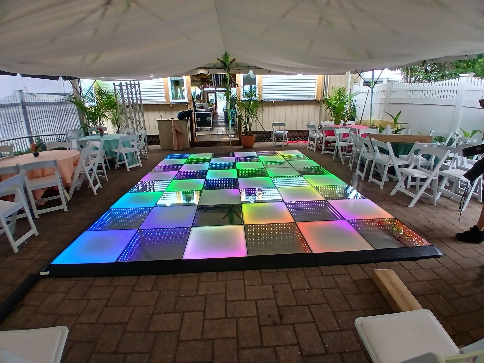 Lighted dance floor under a canopy, surrounded by tables and chairs, outdoor setting.
