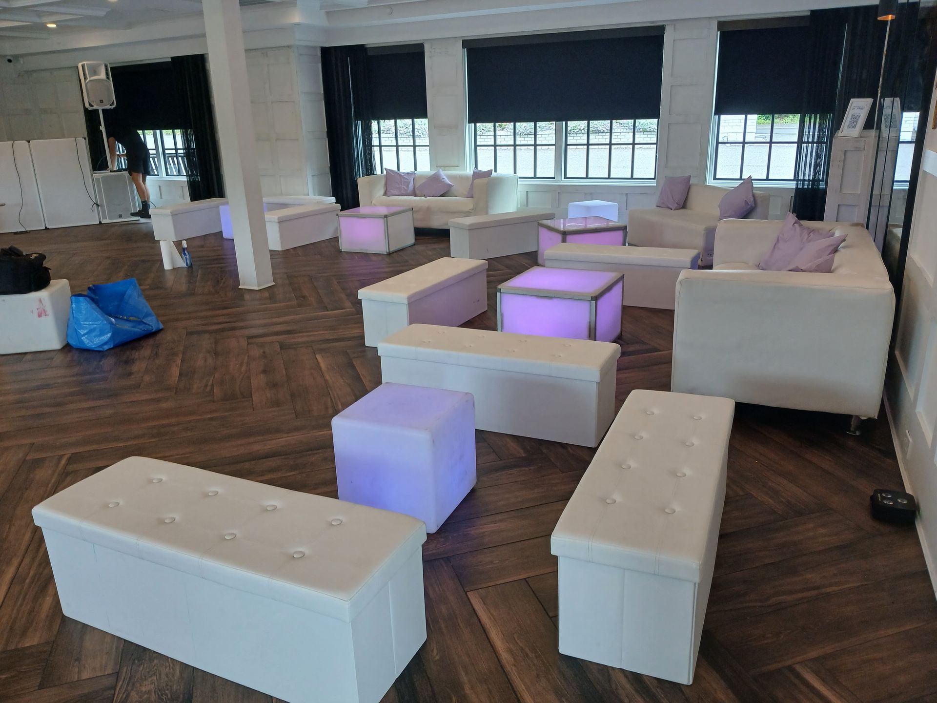 Event space with white furniture, some illuminated in purple, on a wood floor.