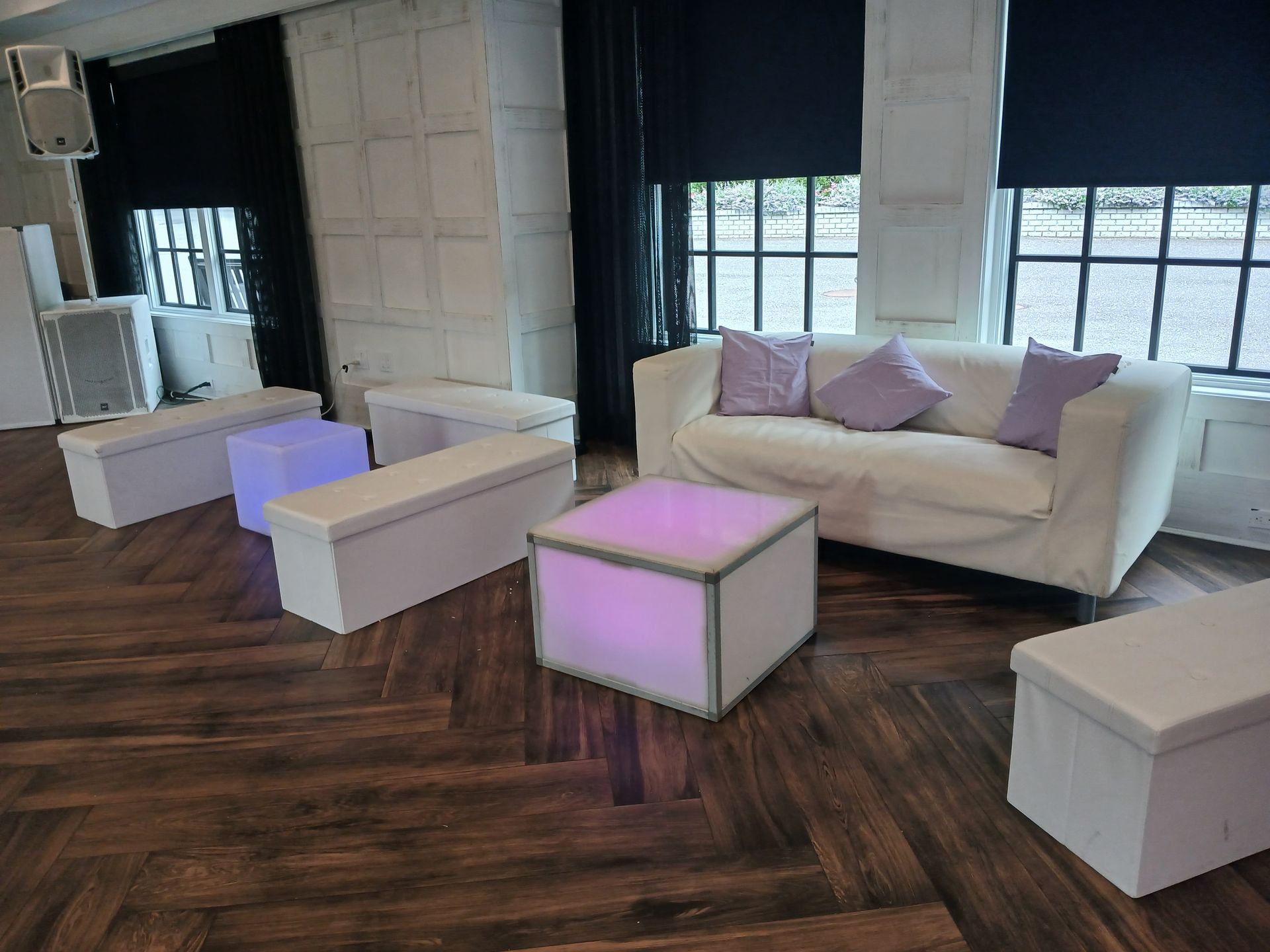 Lounge area with white sofa, ottomans, and accent lighting on a dark wood floor.