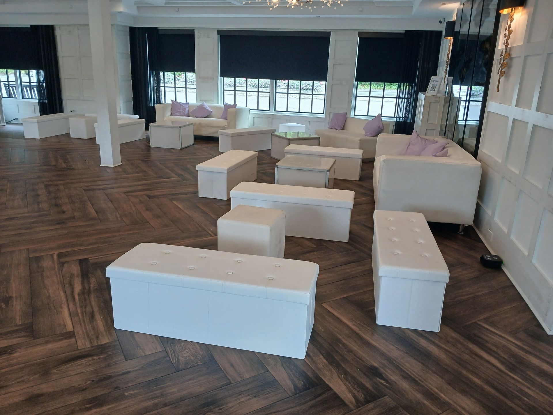 White furniture in a bright room with dark wood floors, including couches, ottomans, and storage benches.