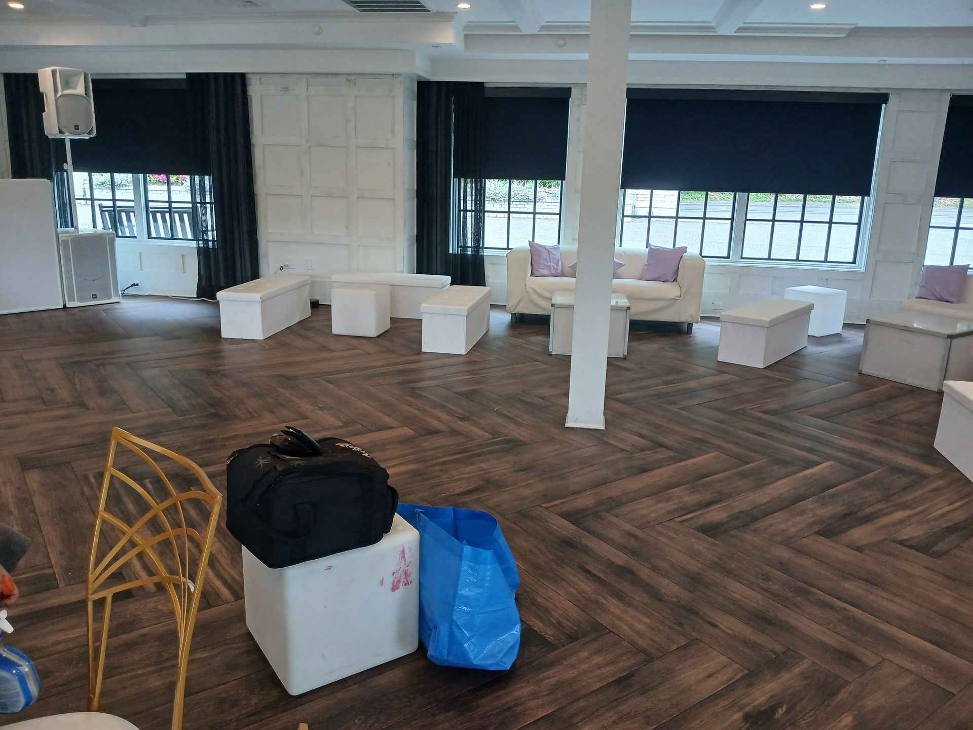 Room with modern furniture: white benches, sofas, coffee tables, dark wood floor, large windows, black blinds.