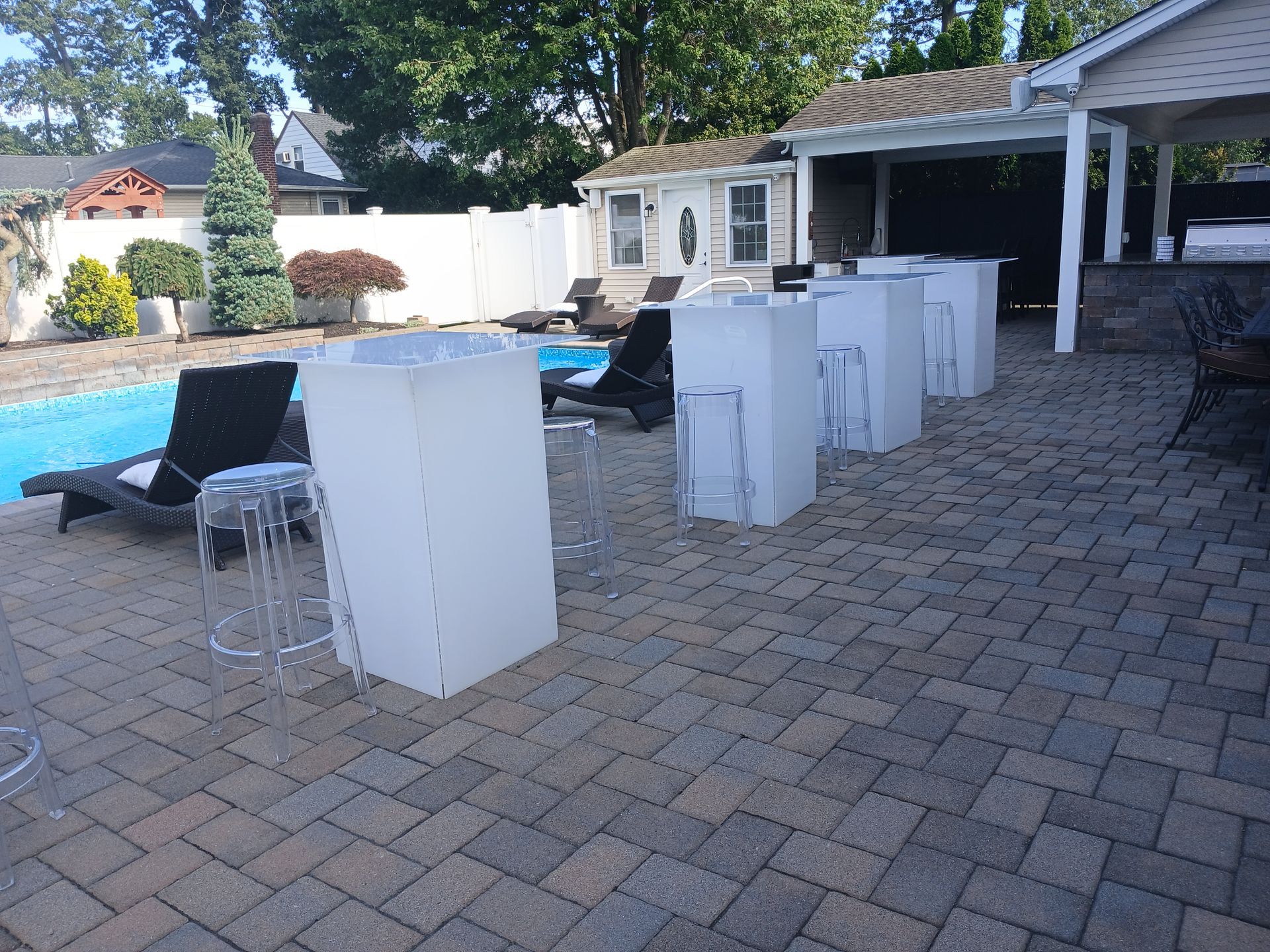 Patio with pool, bar-height tables and stools on brick pavers.