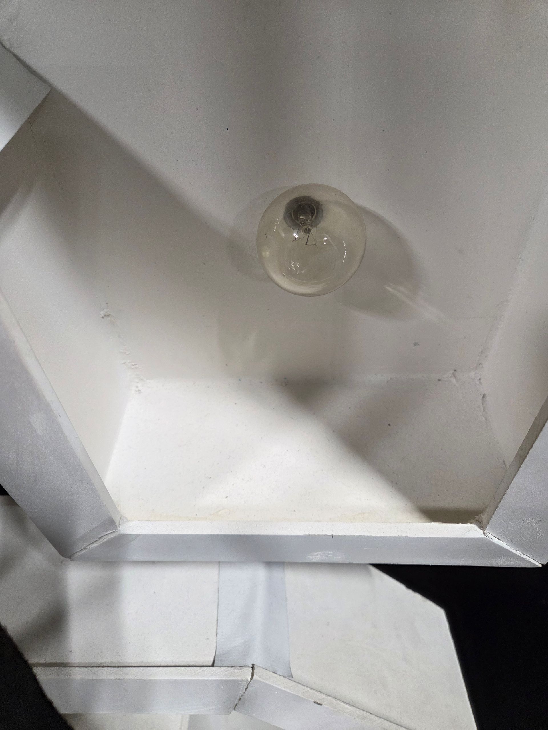 White, angular light fixture with a round lightbulb at its center, casting shadows on the interior.