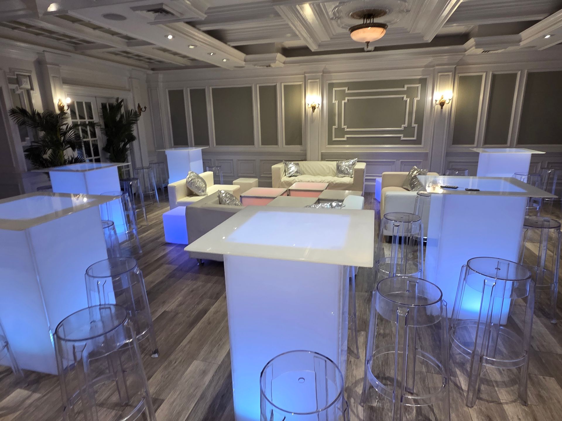 Event space with illuminated tables and chairs. White walls and sofas.