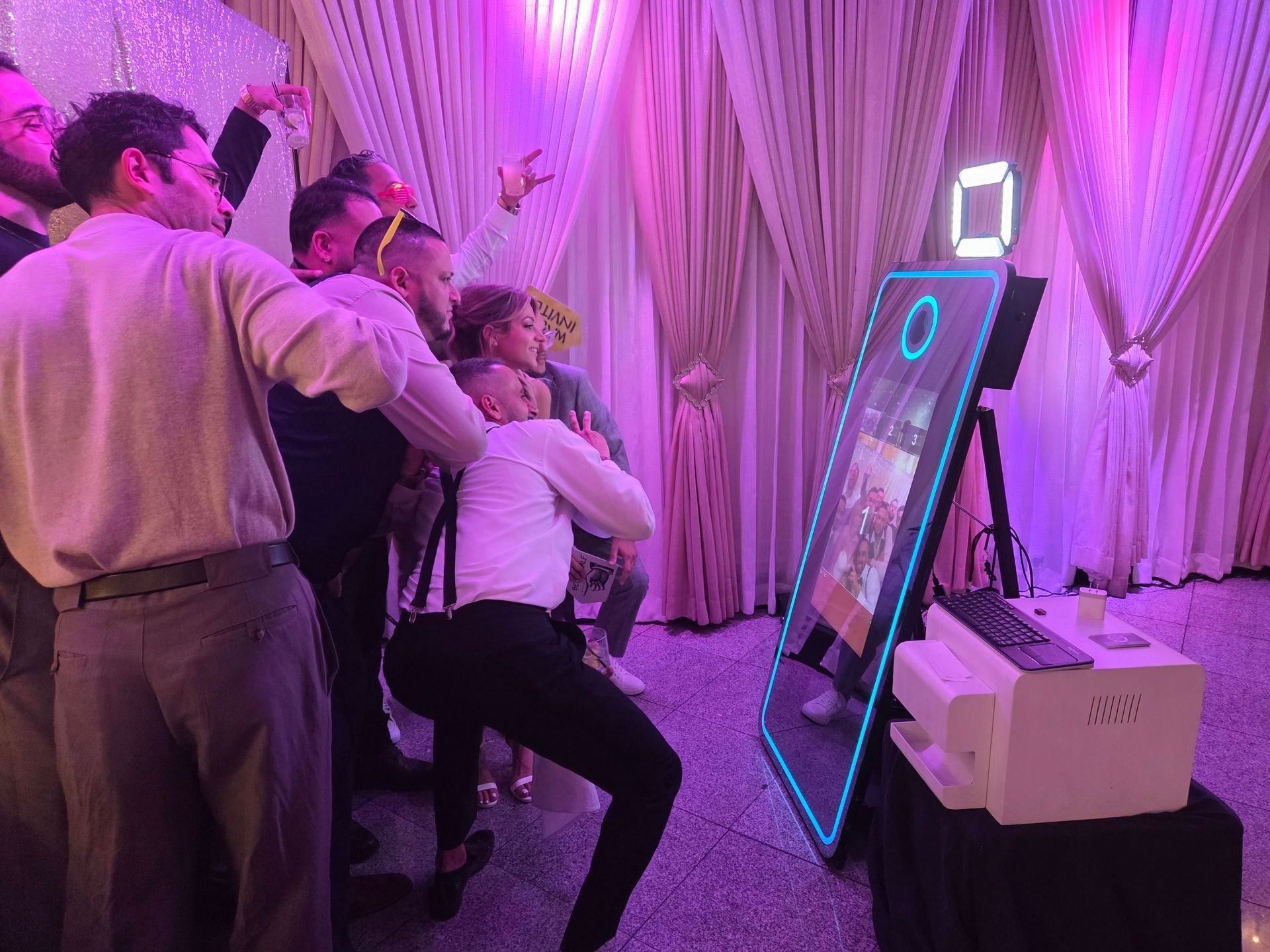 People posing and taking pictures with a mirror photo booth at an event with purple lighting.