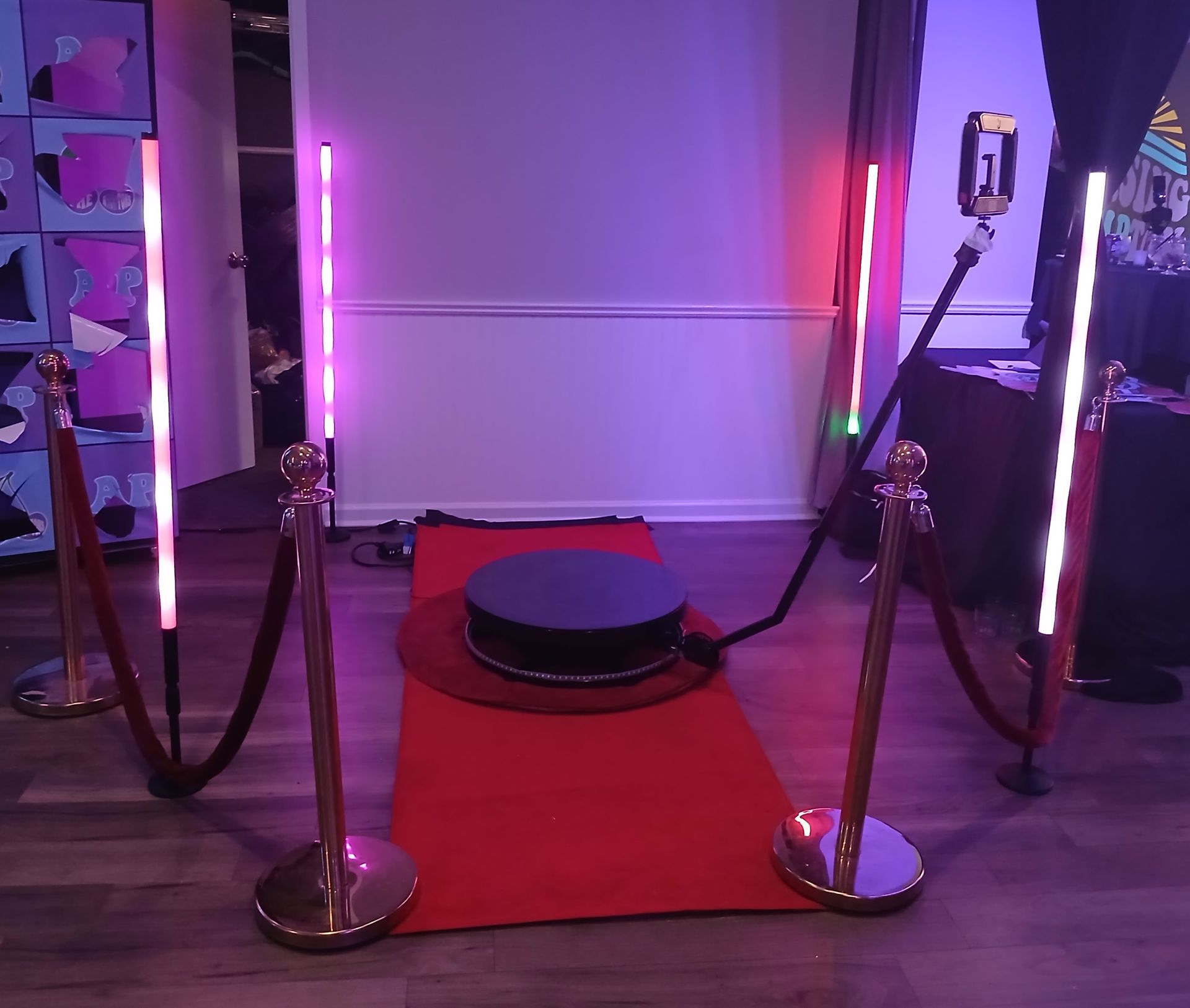 360 photo booth setup with red carpet, ropes, and colorful lights.