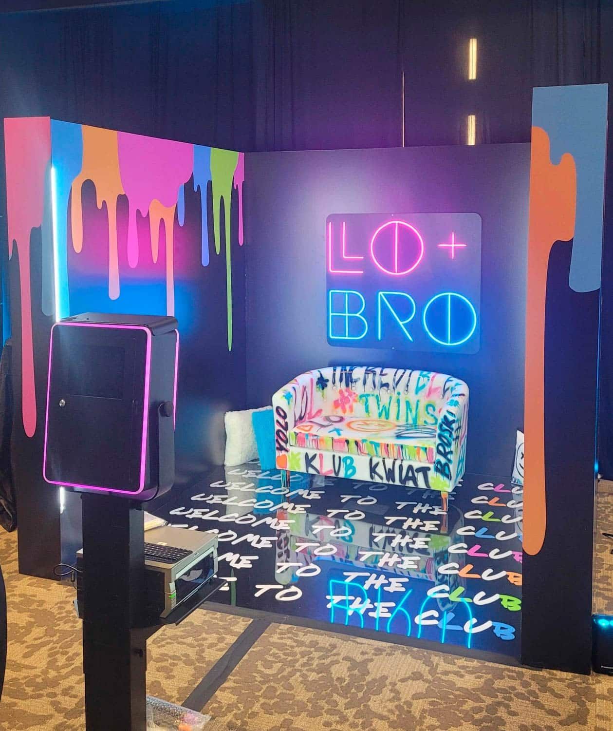Photo booth with graffiti-style backdrop and neon signs. Features a sofa and a photo camera.