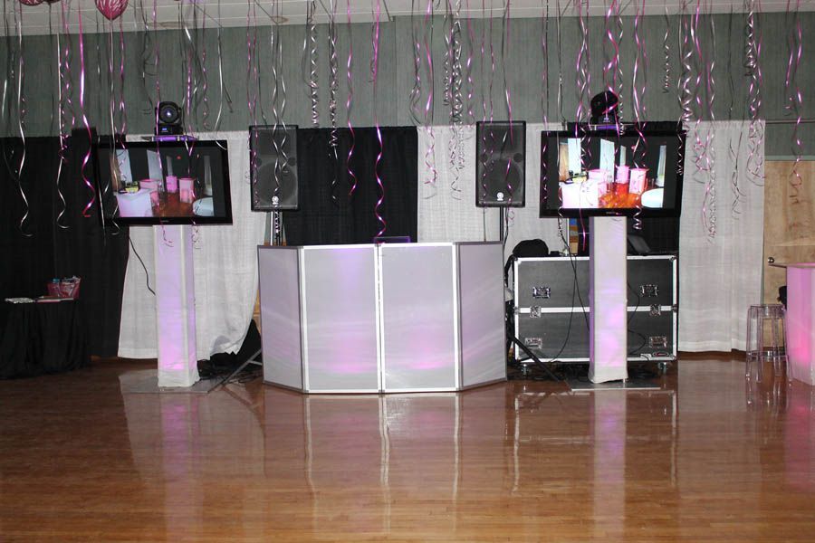 DJ setup with speakers, screens, and pink lighting against a backdrop in a party setting.