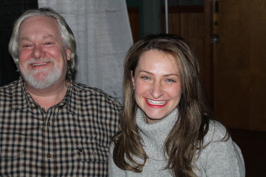 A smiling woman in a gray sweater stands next to a smiling man in a plaid shirt.