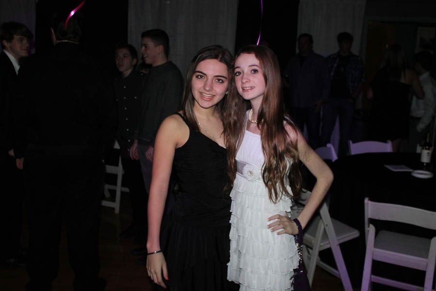Two young women posing at a party; one in a black dress, the other in a white fringed dress.