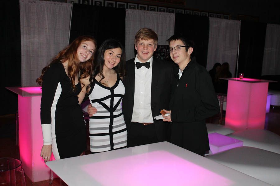 Four formally dressed people pose near glowing tables, black and white outfits.