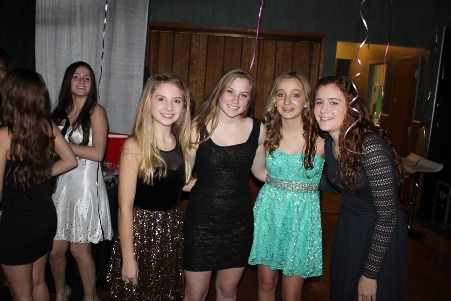 Four young people smiling in formal dresses, posing together at an event.