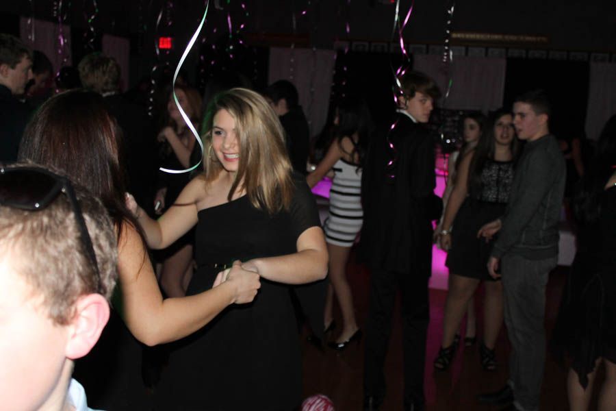 People dancing at a party, in a dark room with lights and streamers. Woman in a black dress smiling and holding hands.