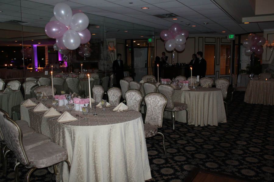Event hall with round tables, chairs, and balloons in shades of pink and white.