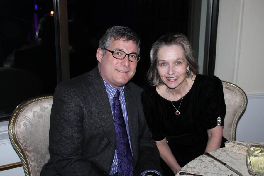 Man and woman smiling at a table indoors, man in suit, woman in black dress.