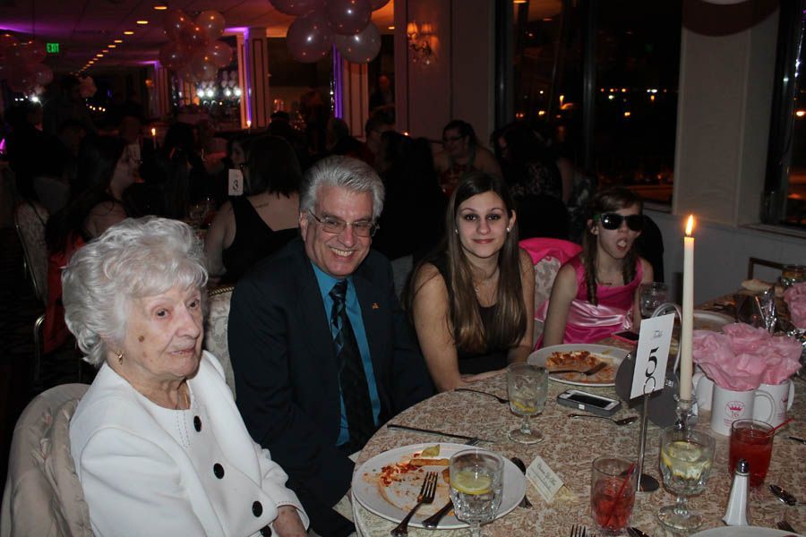 People at a formal dinner table, including an elderly woman, a man in a suit, and two young girls.