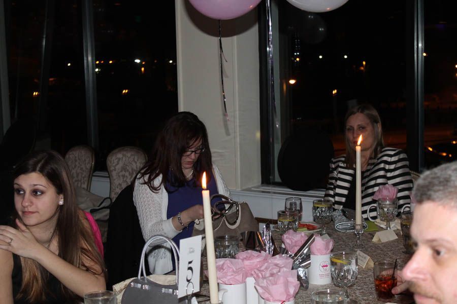 People seated at a table near a window, lit candles, pink and brown balloons.