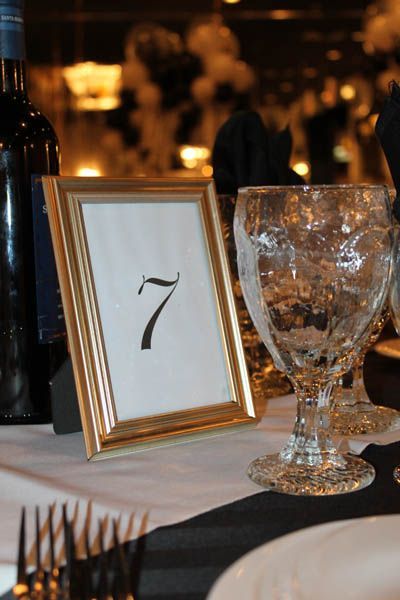 Golden framed table number seven on a formal dining table with glassware and wine bottle.