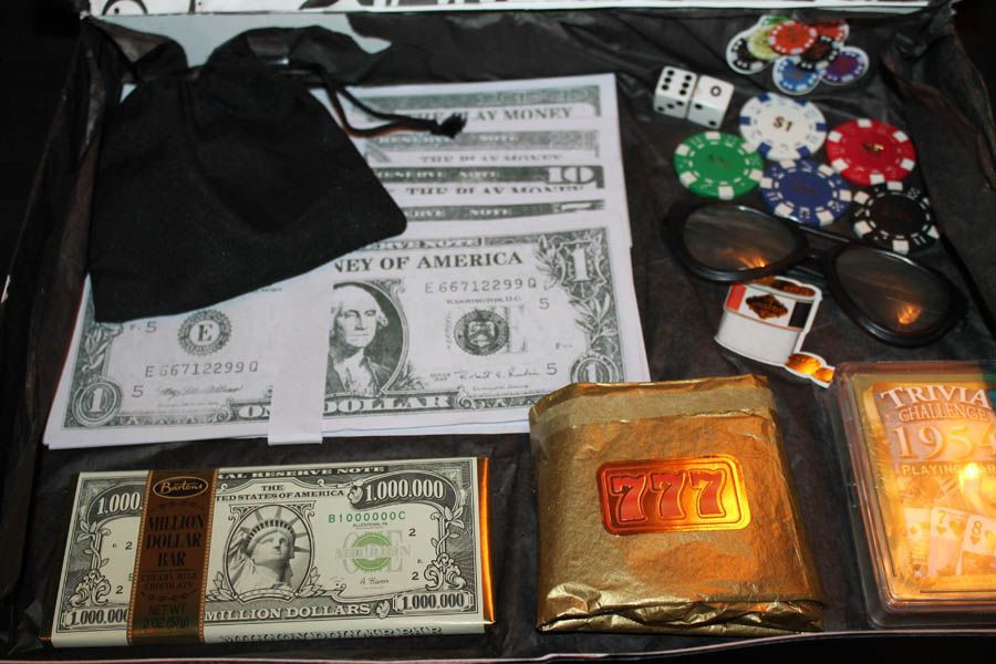 Casino-themed items: toy money, chips, dice, gold bars, sunglasses, and a lighter arranged in a box.