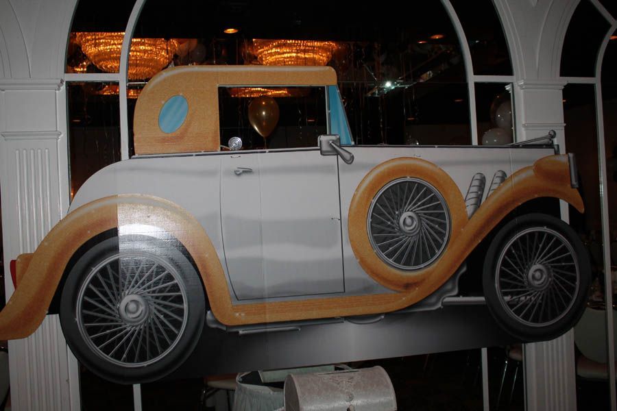 Cardboard cutout of a classic car, white with tan accents, possibly for decoration.