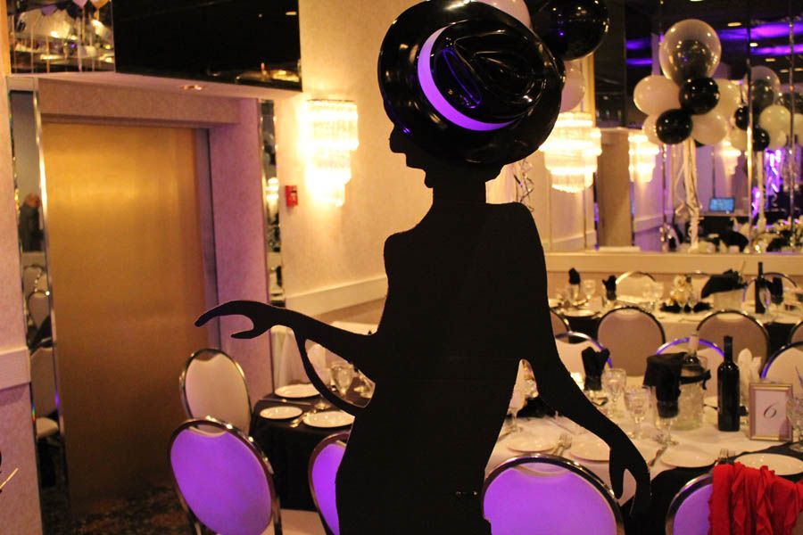 Silhouette of a woman in a large hat at a decorated party table with black and white balloons.