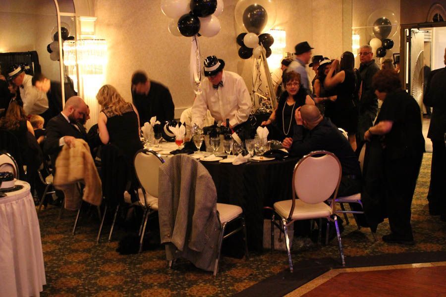 People in formal attire at a party with black, white, and gold decorations, including balloons.