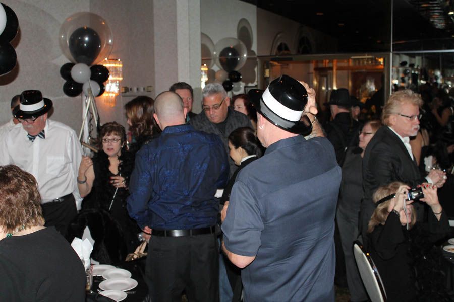 People at a party, some wearing hats. Black and white balloons decorate the room.