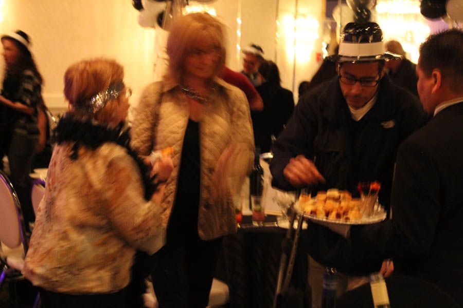 People at a gathering; one holding a plate of food, others in coats, some wearing party hats.