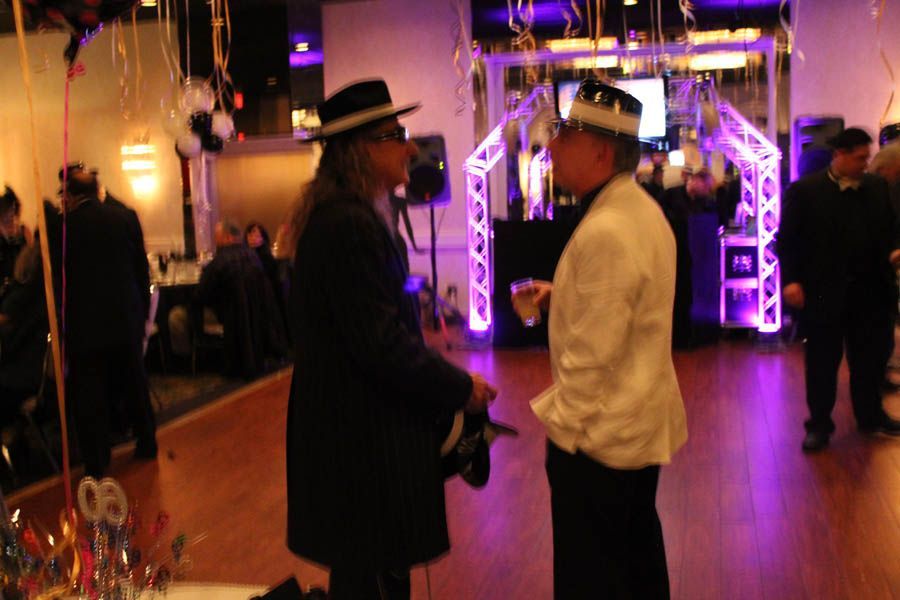 Two men in hats converse at a party with purple lighting and decorations.