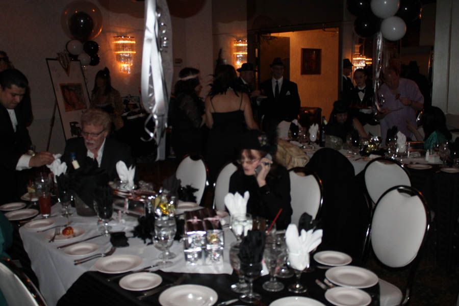 Gatsby-themed event: people at tables, formal attire, black and white decorations, balloons, dining room setting.
