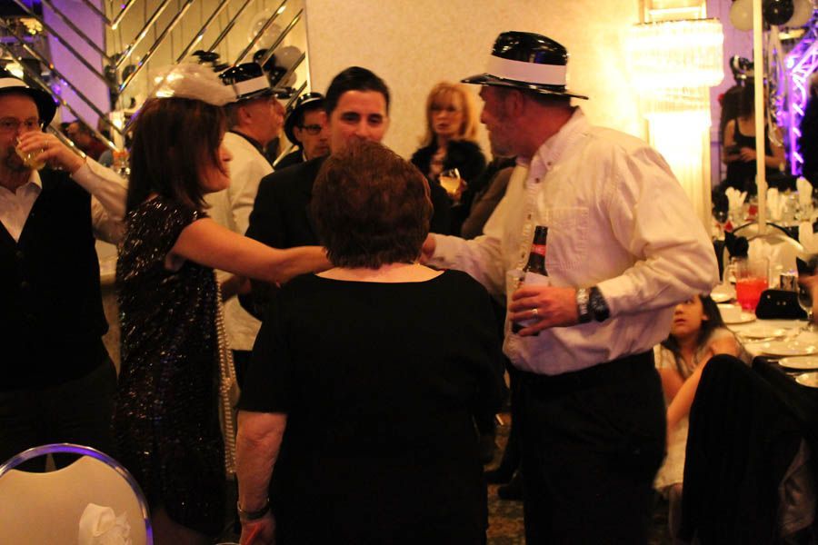 People in festive attire at an event, some wearing hats, toasting and interacting in a brightly lit room.