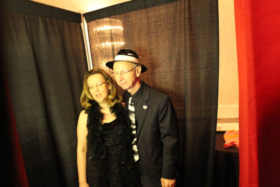 Couple in a photo booth; woman in black outfit with feather boa, man in suit and fedora.