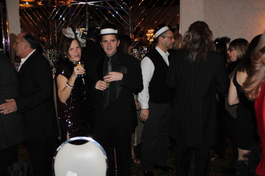 People in formal attire at a party; woman in a sequined dress, men in suits and sailor hats.