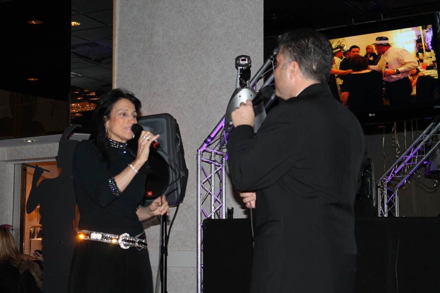 Two people singing into microphones onstage; dark clothing; venue with screens.