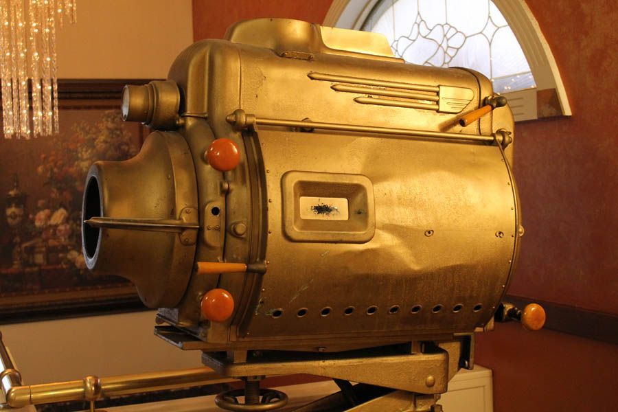 Gold, vintage movie projector, mounted, indoors, near a window.