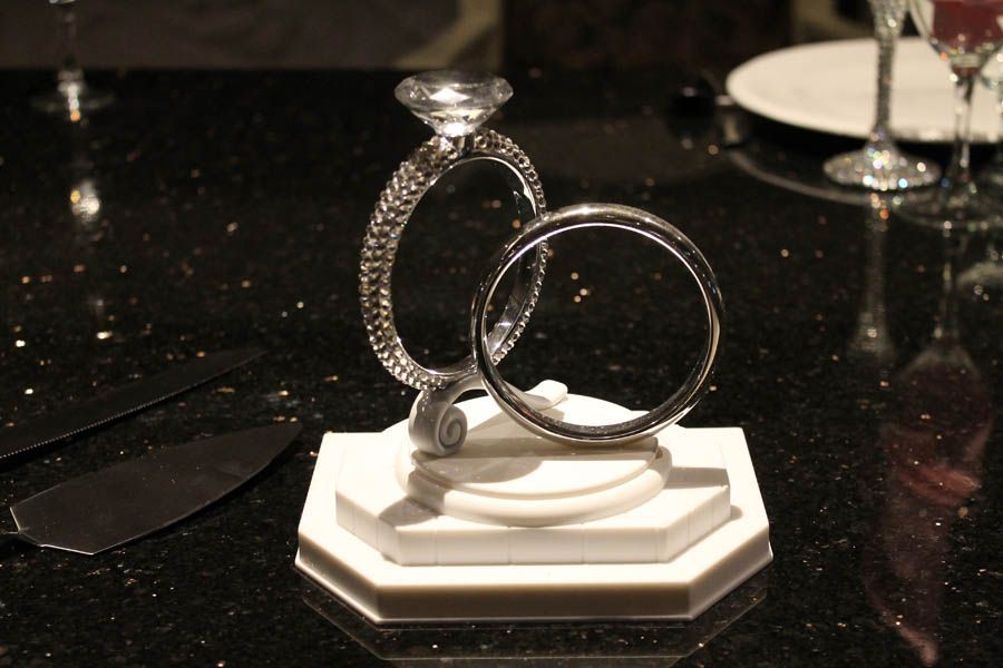 Two diamond rings displayed on a white stand on a dark, speckled surface.