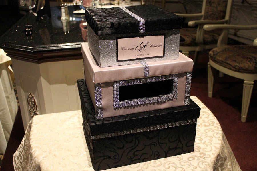 Three decorated boxes stacked on top of each other, on a table. Black and light pink with silver trim.