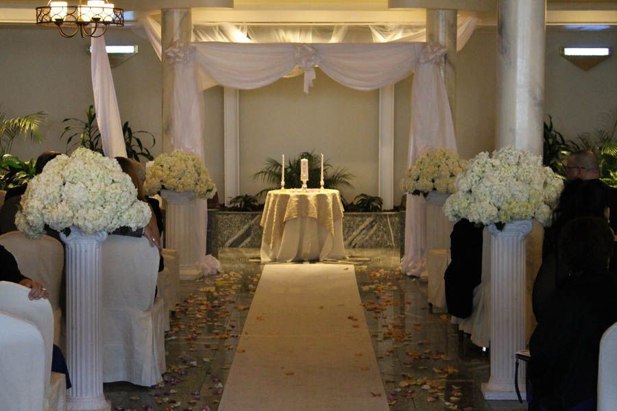 Wedding ceremony setup with white floral arrangements, draped archway, and aisle.