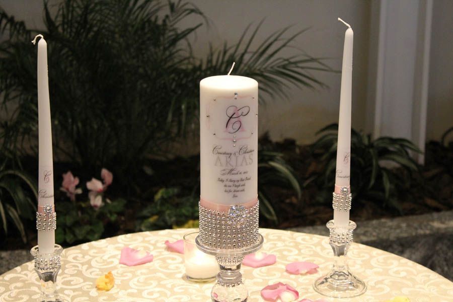 Wedding unity candle set with decorated pillar candle, two taper candles, and rose petals on a table.