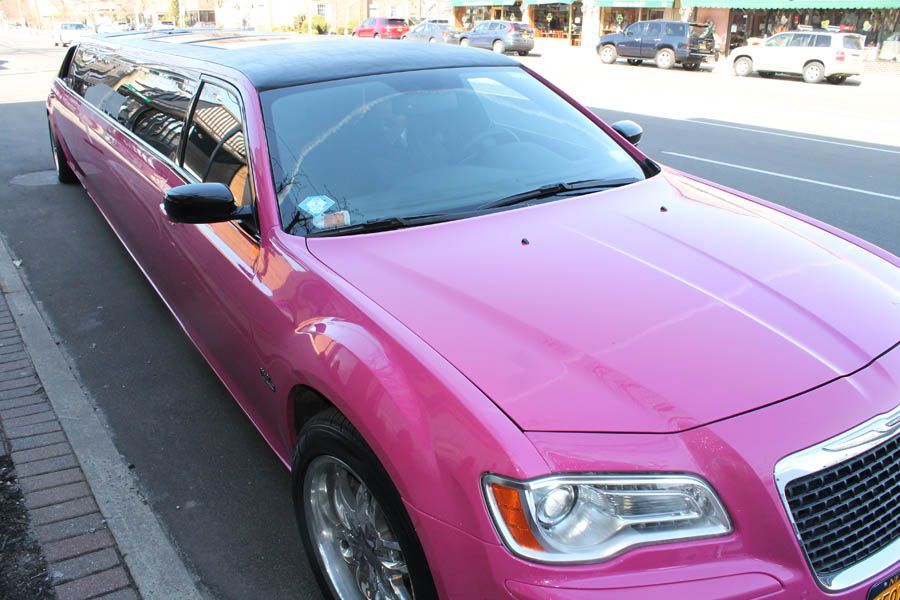 Pink Chrysler 300 limousine parked on a city street. Black roof, chrome wheels.