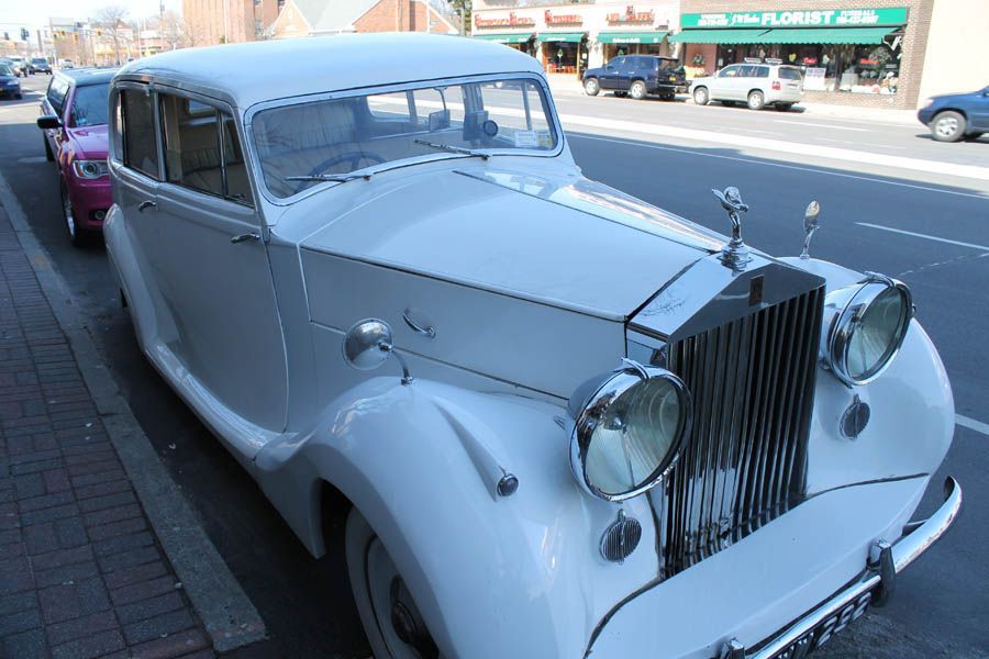 White vintage Rolls Royce parked on a street next to the sidewalk.