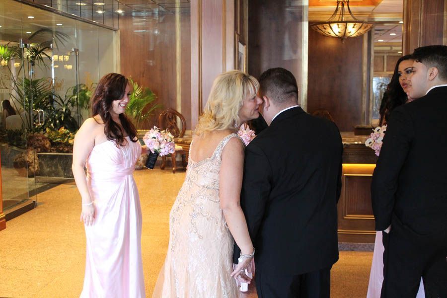 Wedding party: couple kissing, bridesmaid in pink dress, others in formal attire, indoor setting.